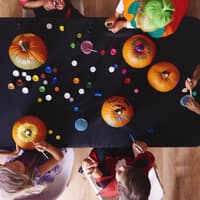 Kinder sitzen am Tisch und bemalen Kürbisse.