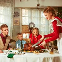 Frau im roten Kleid serviert ihrer Familie einen Braten.