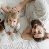 Eltern liegen mit Baby auf dem Bett und machen Quatsch.