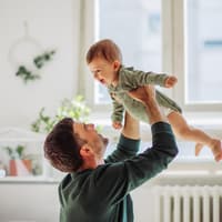 Papa hebt lachendes Baby in die Luft.