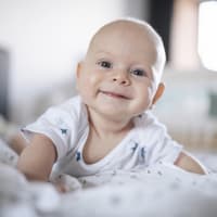 Lächelndes Baby liegt auf dem Bauch.