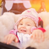 Lachendes Baby in Lammfell-Fußsack im Kinderwagen.