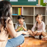 Lehrerin sitzt mit Grundschulkindern auf dem Boden.
