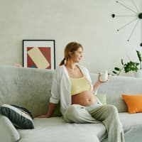 Schwangere Frau trinkt Buttermilch auf dem Sofa.