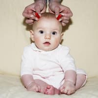 Baby bekommt rote Hörner an die Stirn gehalten.