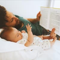 Vater liest Baby im Bett vor.