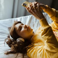 Frau im Bett am Handy mit Kopfhörern.