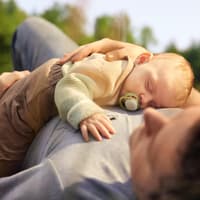 Schlafendes Baby mit Schnuller liegt auf Papas Bauch.