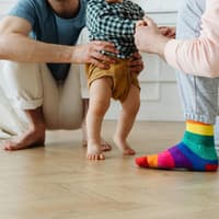 Baby läuft barfuß mit Hilfe von einem zum anderen.