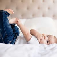 Ein kleines Baby mit Jeans liegt auf einem Bett. 