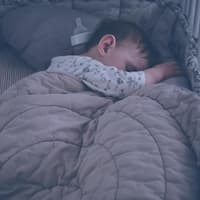 Baby im Bett mit Nestchen und Decke.
