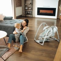 Mutter sitzt mit Baby auf dem Boden neben einer Babywippe.
