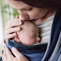 Mutter hat kleines Baby im Tragetuch und kuschelt zärtlich mit ihm.