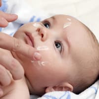 Babys Gesicht wird eingecremt.