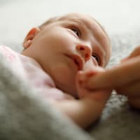 Müdes Baby hält Finger eines Elternteils.