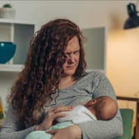 Frau stillt mit schmerzverzerrtem Gesicht ihr Baby.