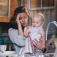 Mutter mit Baby auf dem Arm schlägt die Hand überm Kopf zusammen.