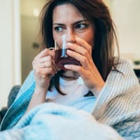 In Decke gehüllte Frau trinkt einen Tee.