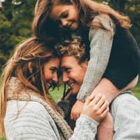 Ein junges Pärchen schaut sich in die Augen, während die gemeinsame Tochter auf den Schultern des Vaters sitzt.