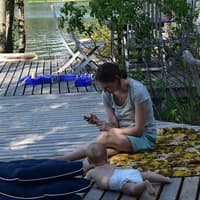 Mutter mit Baby am Wasser mit Handy in der Hand.