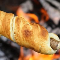 Ein Stockbrot aus Pizzateig wird am Lagerfeuer gegrillt. 