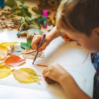 Kinder basteln mit Herbstblättern und Stiften.