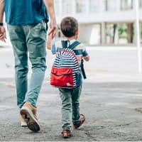 Vater geht mit kleinem Kind an der Hand zur Schule.