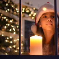 Ein Mädchen schaut aus einem weihnachtlichen Fenster.