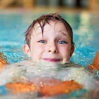 Kind mit Schwimmnudel im Wasser.