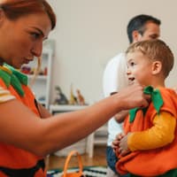 Frau passt Kind ein Kürbiskostüm an.