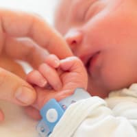 Eine Mama streichelt die Hand ihres neugeborenen Babys
