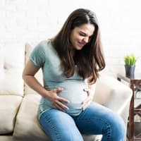 Eine schwangere Frau mit schmerzverzerrtem Gesicht hält ihren Babybauch. 