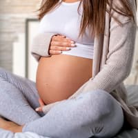 Schwangere Frau sitzt im Schneidersitz und hält sich den Bauch.