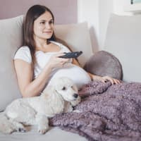 Schwangere Frau mit Hund zappt im Fernseher.