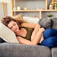 Frau liegt mit Bauchschmerzen auf dem Sofa.