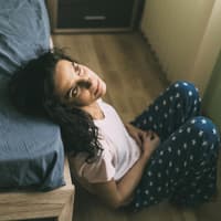 Frau sitzt vorm Bett und starrt an die Decke.
