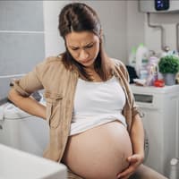 Schwangere Frau mit Schmerzen auf der Toilette.