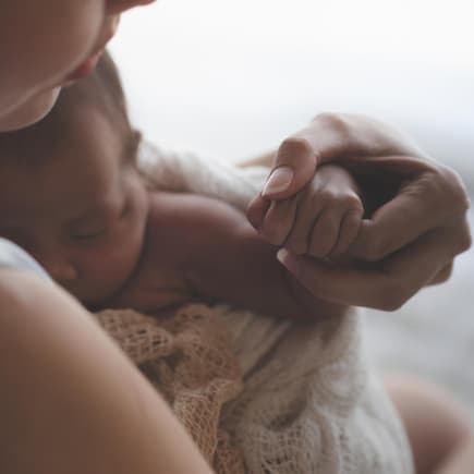 Mutter hält ihr Neugeborenes eingewickelt im Arm
