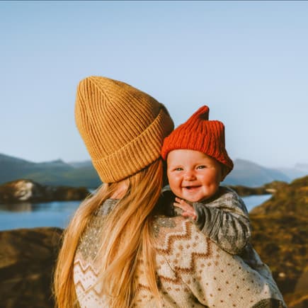 Ein Mutter hält ihr Baby und beide tragen einen Norweger-Pulli. 