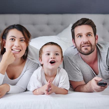 2-Jähriger guckt mit seinen Eltern einen Kinderfilm vom Bett aus