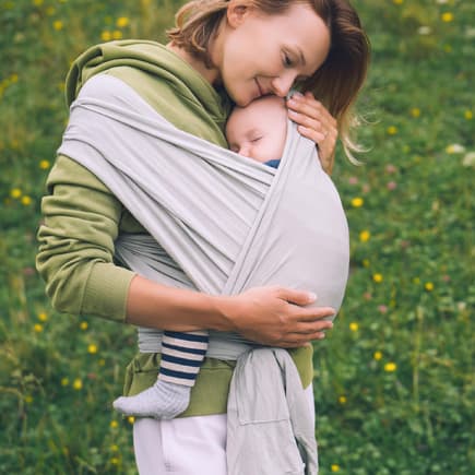 Frau trägt ihr Baby in einer Trage.
