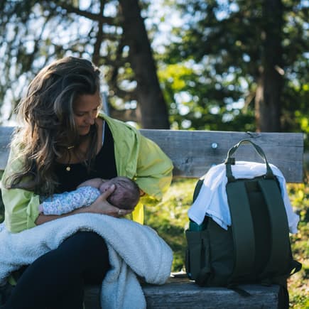 Eine Frau, die ihr Baby auf einer Bank im Grünen stillt.
