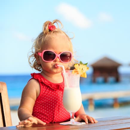Ein kleines Mädchen mit rotem Badeanzug und Sonnenbrille trinkt einen Kinder-Cocktail.
