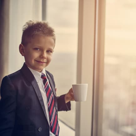 Ein Junge steht im Anzug am Fenster mit einer Kaffeetasse. 