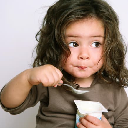 Kleinkind löffelt einen Joghurt.