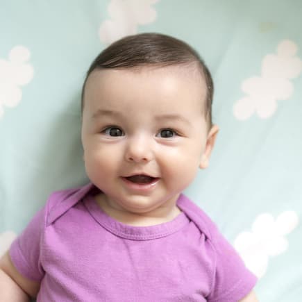 Ein Baby liegt lächelnd auf einer Decke mit kleinen Wolken. 