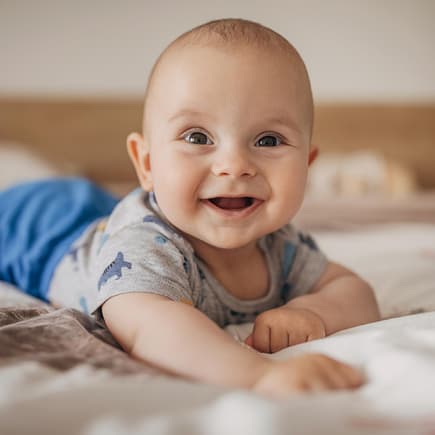 Ein Baby liegt lachend auf dem Bauch.