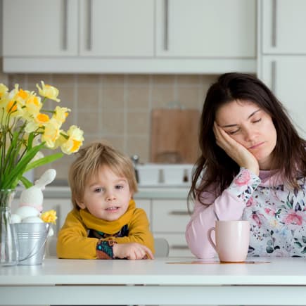 Mama sitzt müde am Tisch, Kind ist hellwach