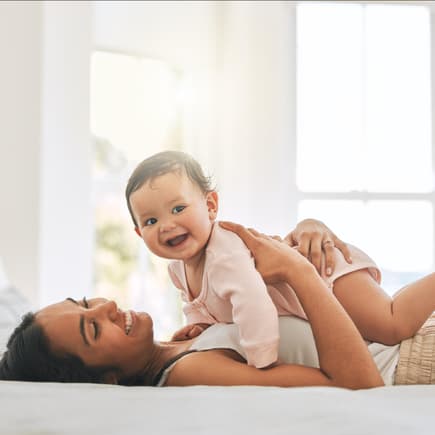 Ein Baby liegt lachend auf dem Bauch seiner Mama.