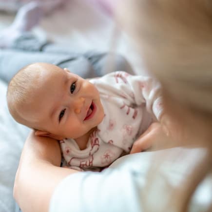 Ein Baby liegt lachend in Mamas Armen.
